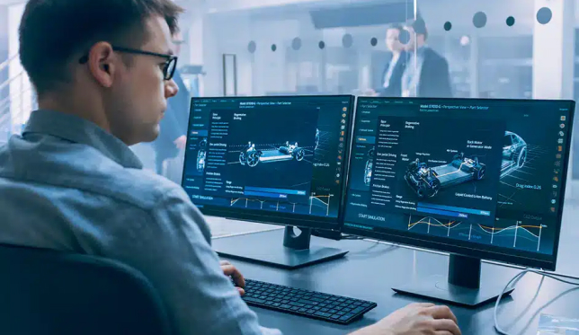 A man analyzes complex engineering data on dual computer monitors in a modern federal office setting.